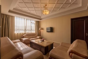 Ein Hotelzimmer mit großem Fenster, einem Flachbildfernseher, einem Holztisch und beigen Ledersofas.
