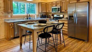 A modern kitchen with wooden cabinetry, stainless steel appliances, and a large island with bar stools. - Beautiful Mountain View - Charming 2-bedroom house in Murphy, NC (Murphy)