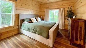 A wooden cabin bedroom with a bed, a ceiling fan, a window, and a nightstand. - Beautiful Mountain View - Charming 2-bedroom house in Murphy, NC (Murphy)