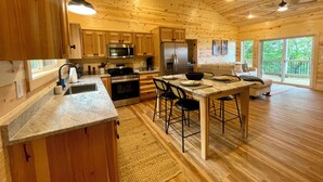 A spacious wooden cabin interior with a kitchen, dining area, and a large sliding glass door to a deck. - Beautiful Mountain View - Charming 2-bedroom house in Murphy, NC (Murphy)