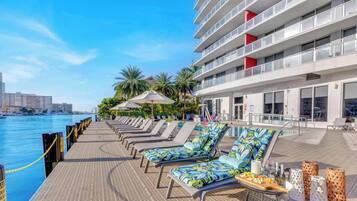A poolside area with lounge chairs, umbrellas, and a view of the water.