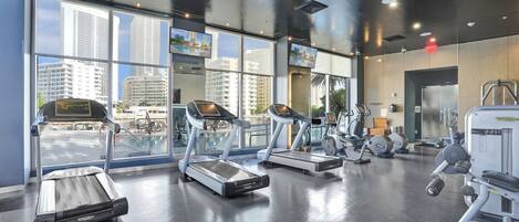 A gym with treadmills, weight machines, and large windows offering city views.