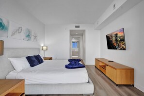 Une chambre d’hôtel moderne avec un lit, une table de chevet en bois, un téléviseur et un tableau représentant un paysage urbain accroché au mur.