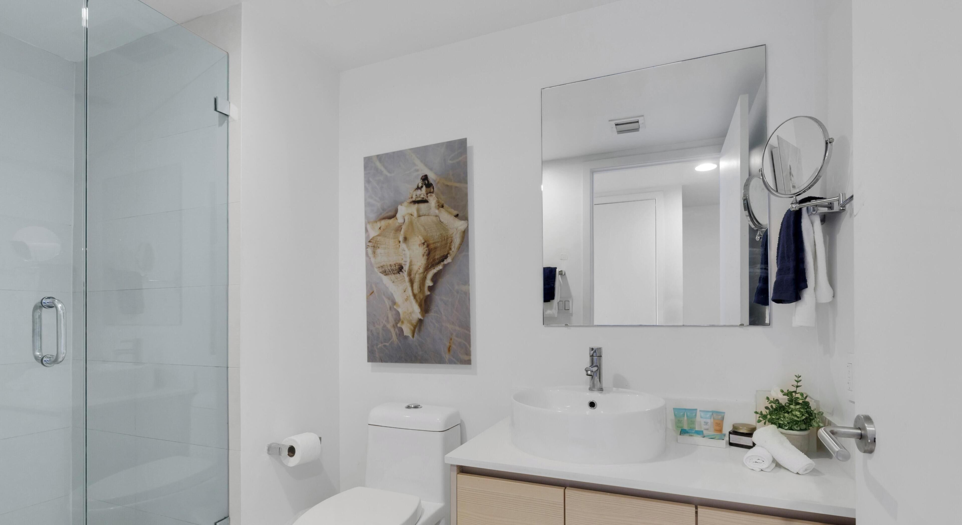 Une salle de bain moderne avec une douche à parois de verre, des toilettes, un lavabo avec un miroir et un porte-serviettes fixé au mur.