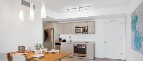 Una cocina moderna con electrodomésticos de acero inoxidable, una zona de comedor con mesa y sillas de madera, e iluminación colgante.