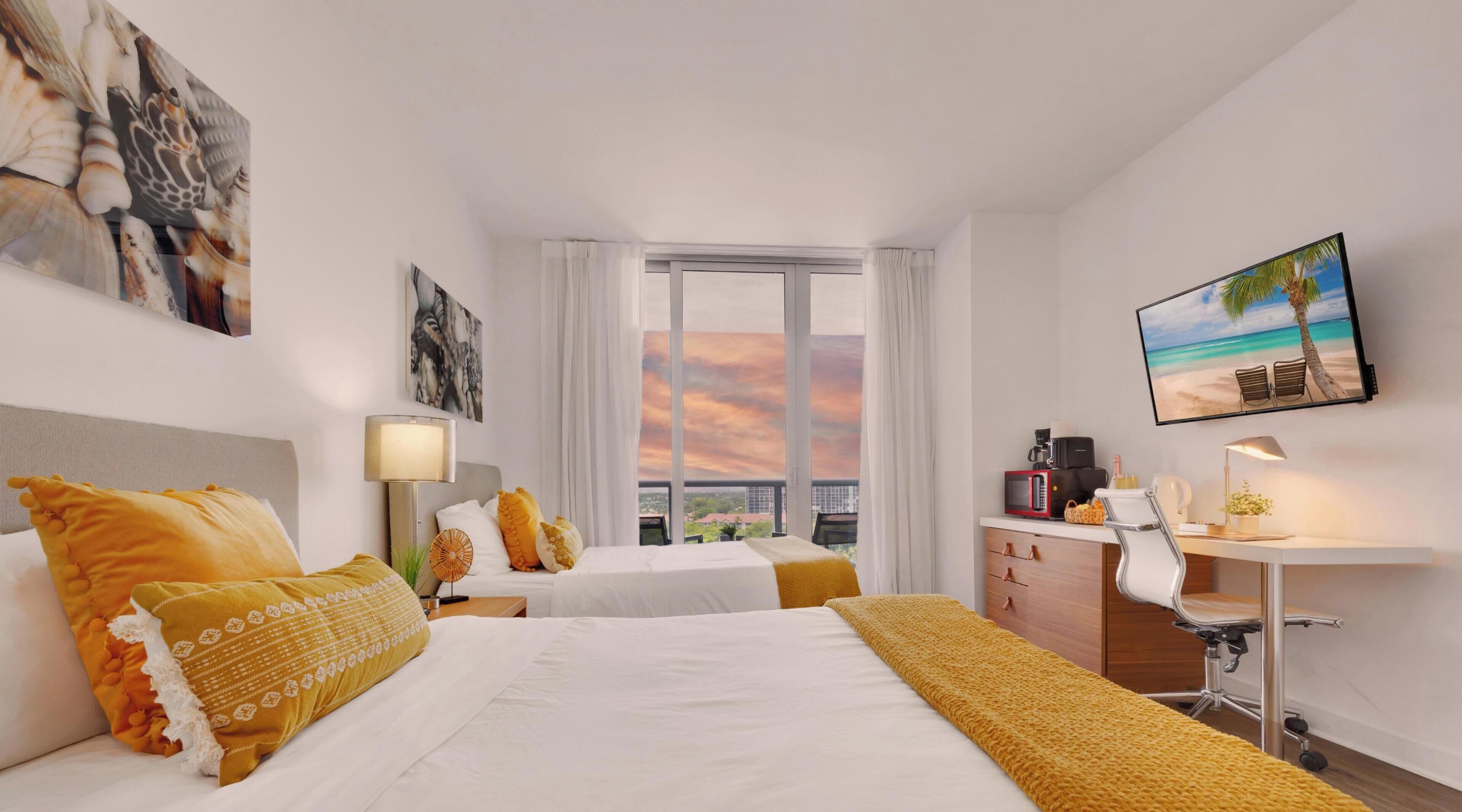 Camera d'albergo con due letti, una scrivania, una sedia, una TV e vista sul cielo.