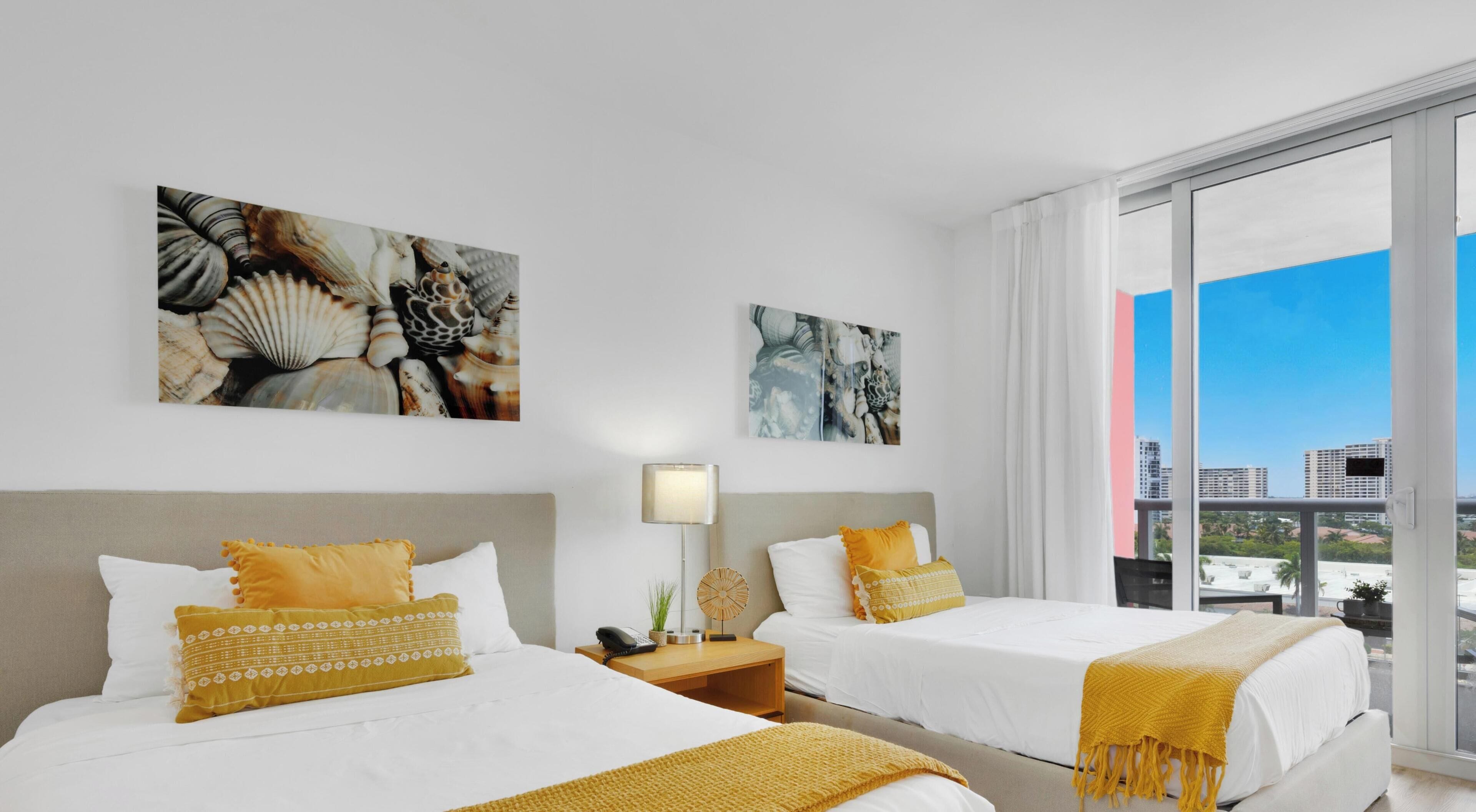 A hotel room with two beds, a large window, and artwork on the walls.