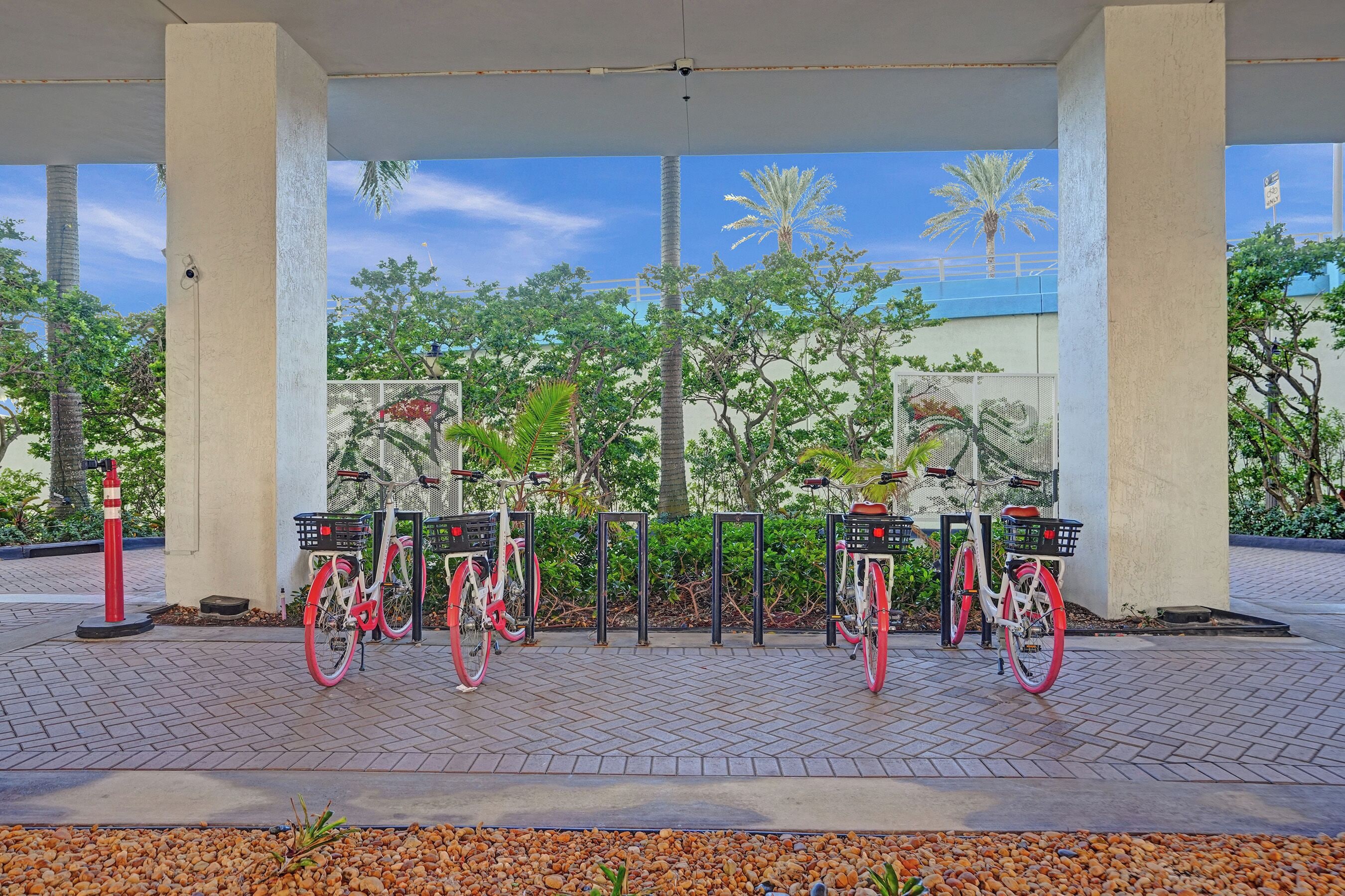 A covered bike parking area with three bicycles, a red bollard, and a concrete pillar.