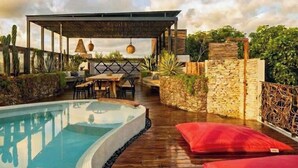 A pool area with a wooden deck, a covered seating area, and a stone wall.