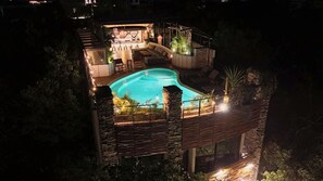 A nighttime view of a pool area with a lounge, seating, and a staircase leading to an upper level.