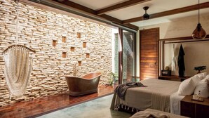 A modern bedroom with a stone wall, a large window, a wooden ceiling, and a bed with a headboard.