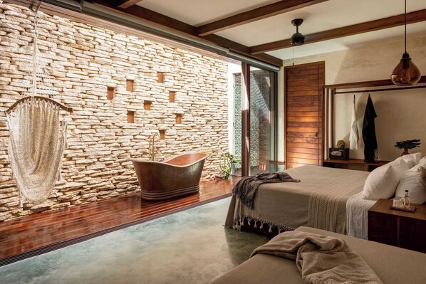 Une chambre à coucher moderne avec un mur en pierre, une grande fenêtre, un plafond en bois et un lit doté d’une tête de lit.