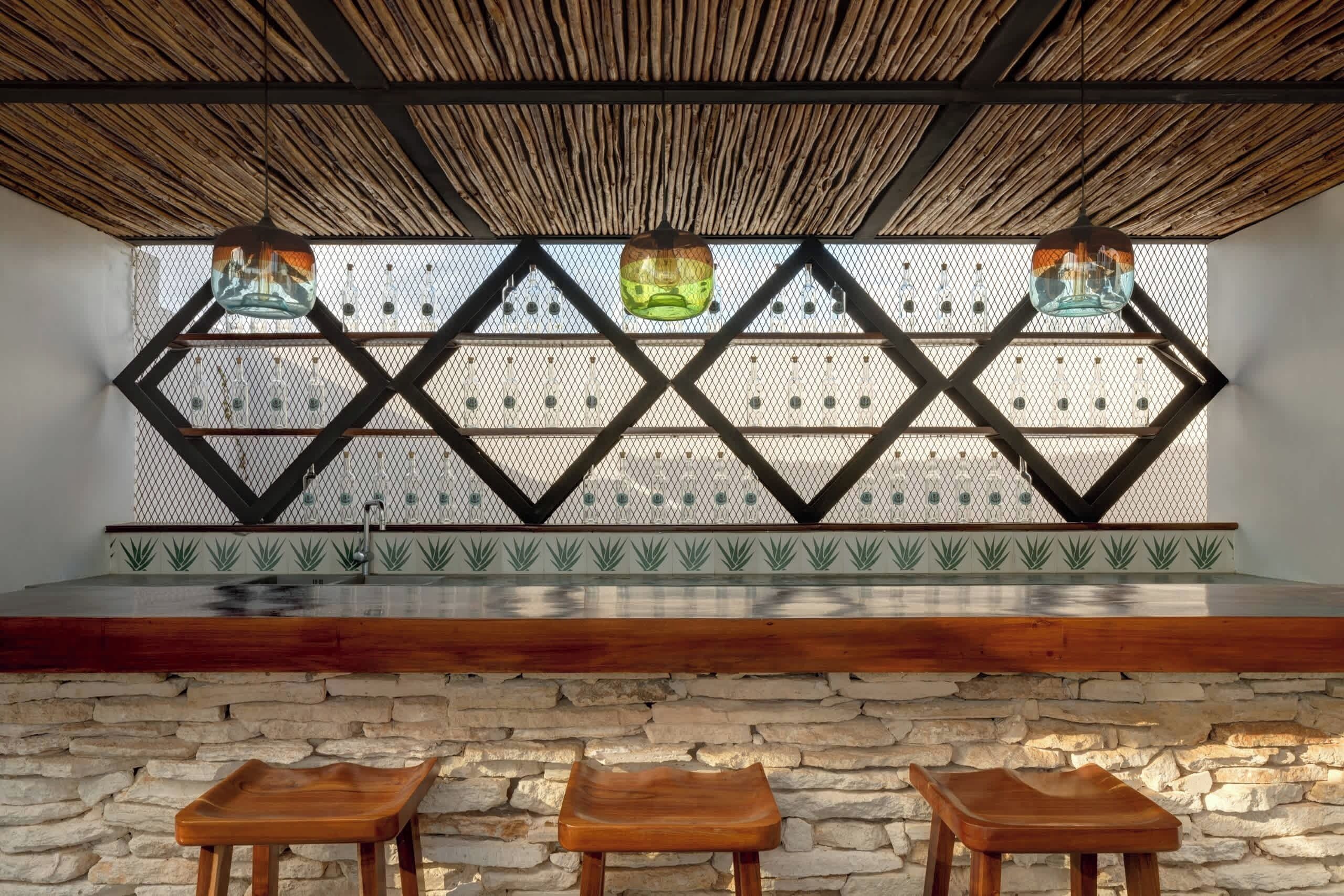 A bar area with a stone wall, wooden stools, and a geometric patterned wall behind the bar.