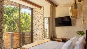 A bedroom with a large bed, a TV mounted on the wall, and a balcony with a stone wall.