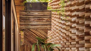 A narrow outdoor corridor with a wooden slatted wall, a brick wall with greenery, and a black woven floor.