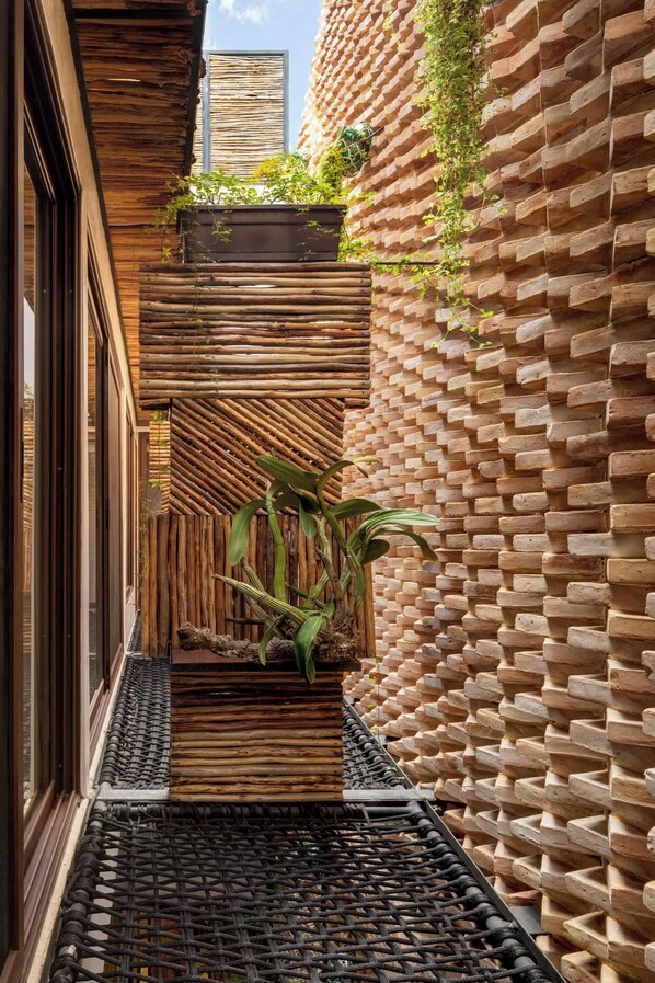 Un étroit couloir extérieur avec un mur en lattes de bois, un mur de briques orné de verdure et un sol en fibres tissées noires.