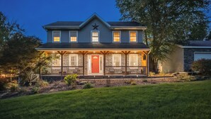 A two-story house with a red door, stone facade, and a porch with railings. - Heated Pool • Hot Tub• Game Room• Fire Pit• 6 Bdrms (Forest City)