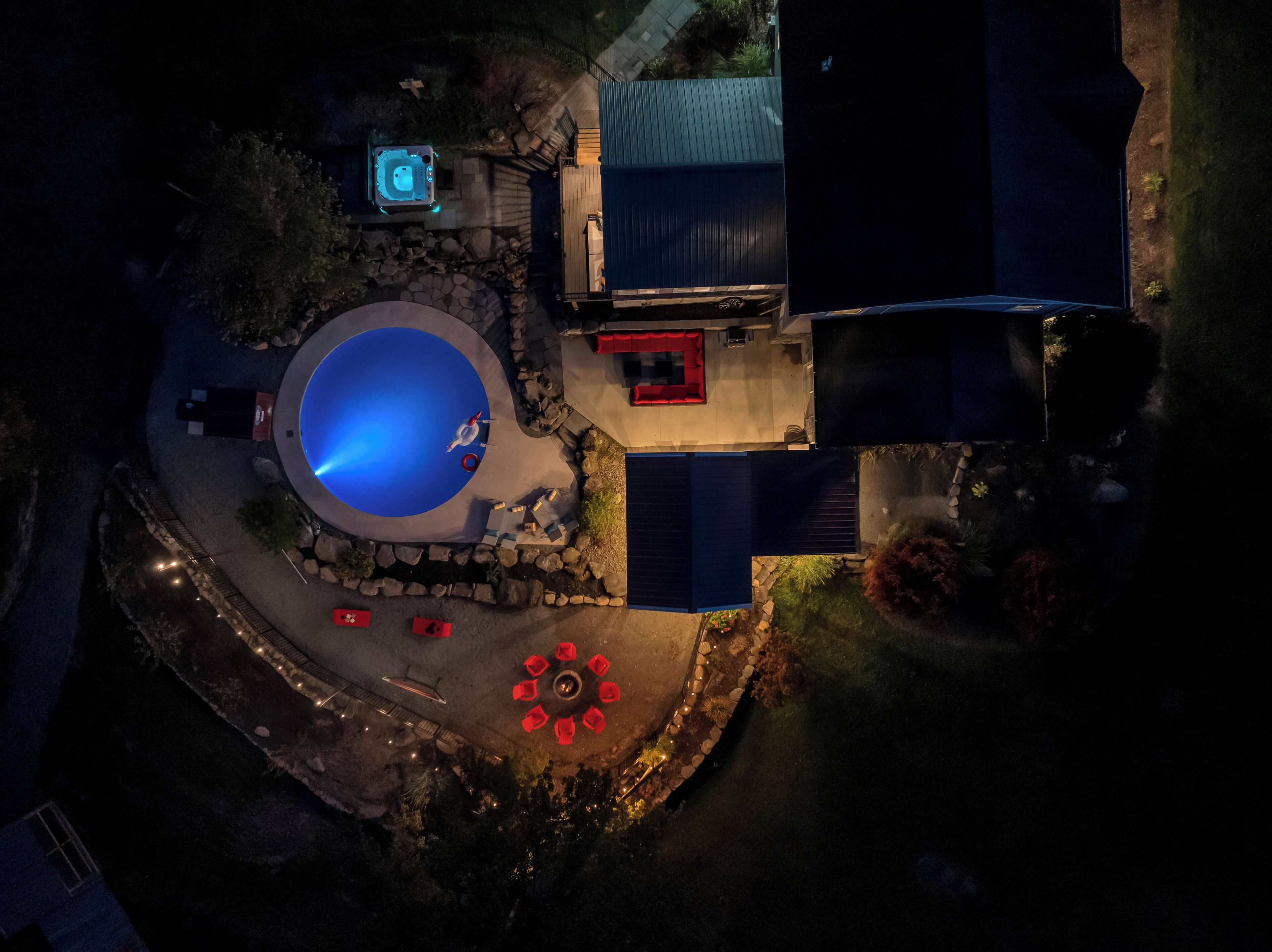 Vista aérea de una propiedad residencial con piscina, jacuzzi y zona de patio con sillas rojas.