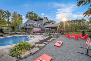 Un patio trasero con piscina, sillas reclinables rojas y un área de terraza techada.