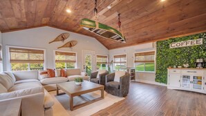 A spacious living area with a wooden ceiling, a green boat-shaped light fixture, a coffee-themed wall, and a view of greenery outside. - Heated Pool • Hot Tub• Game Room• Fire Pit• 6 Bdrms (Forest City)