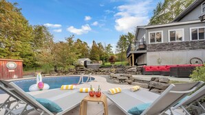 A backyard with a swimming pool, lounge chairs, a red outdoor sofa, and a stone wall. - Heated Pool • Hot Tub• Game Room• Fire Pit• 6 Bdrms (Forest City)