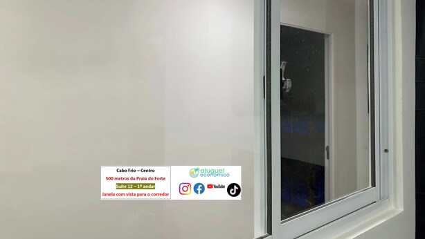 A hotel room with a large window, a white wall, and a door. There is a sign in the bottom left corner with text and logos.