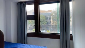 A room with a bed, a window with curtains, and a view of the outside.
