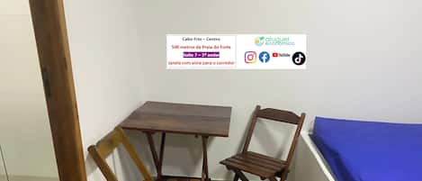 A corner room with a wooden table and two chairs, a blue bed, and a white wall.