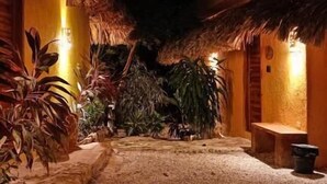 An outdoor area with a thatched roof, surrounded by various plants and a gravel path. - Suites Casa de Piedra y Colores-Sak (Tinum)
