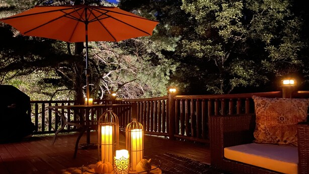 Una terrazza esterna con un divano in rattan, un ombrello rosso e tre lanterne illuminate.