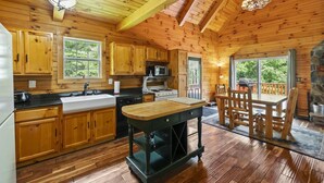 Una cabaña de madera con cocina que cuenta con armarios de madera, una isla central, una mesa de comedor con sillas y una chimenea de piedra.