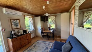 Una habitación acogedora con techo de madera, un sofá azul, una mesa de comedor con sillas y una zona de cocina con microondas y cafetera.