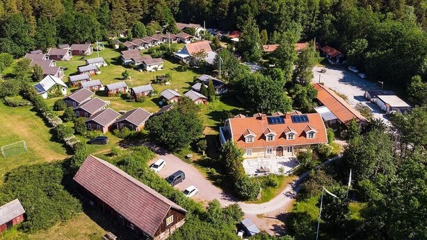 Vista aérea de una zona residencial con casas, un edificio grande con paneles solares y un fondo boscoso.