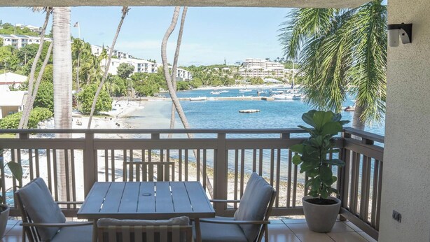 A balcony with a wooden table and chairs, overlooking a beach with boats and palm trees. - SeaDazzle-beachfront, pool, Jeep (St. Thomas)