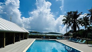 A rectangular swimming pool with a wooden deck surrounding it, lounge chairs, and palm trees in the background. - SeaDazzle-beachfront, pool, Jeep (St. Thomas)