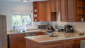 A modern kitchen with wooden cabinets, a large island, stainless steel appliances, and a window providing natural light. - SeaDazzle-beachfront, pool, Jeep (St. Thomas)