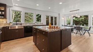 A modern kitchen with a central island, large windows, and a dining area with chairs. - Ski Chalet • 4 bedroom • Beautifully Remodeled • Walk to Lifts (Park City)
