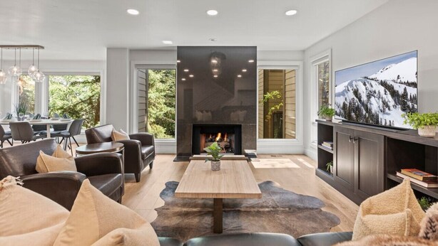 A modern living room with a fireplace, comfortable seating, a large TV, and a dining area with natural light. - Ski Chalet • 4 bedroom • Beautifully Remodeled • Walk to Lifts (Park City)