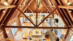 Interior de madera con techos altos, un área de estar central, paredes de piedra y vista al nivel inferior.