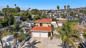 A residential area with two-story houses, palm trees, and a clear sky.