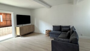 A spacious living room with a large grey sectional sofa, a wooden cabinet with a flat-screen TV, and a wicker basket.