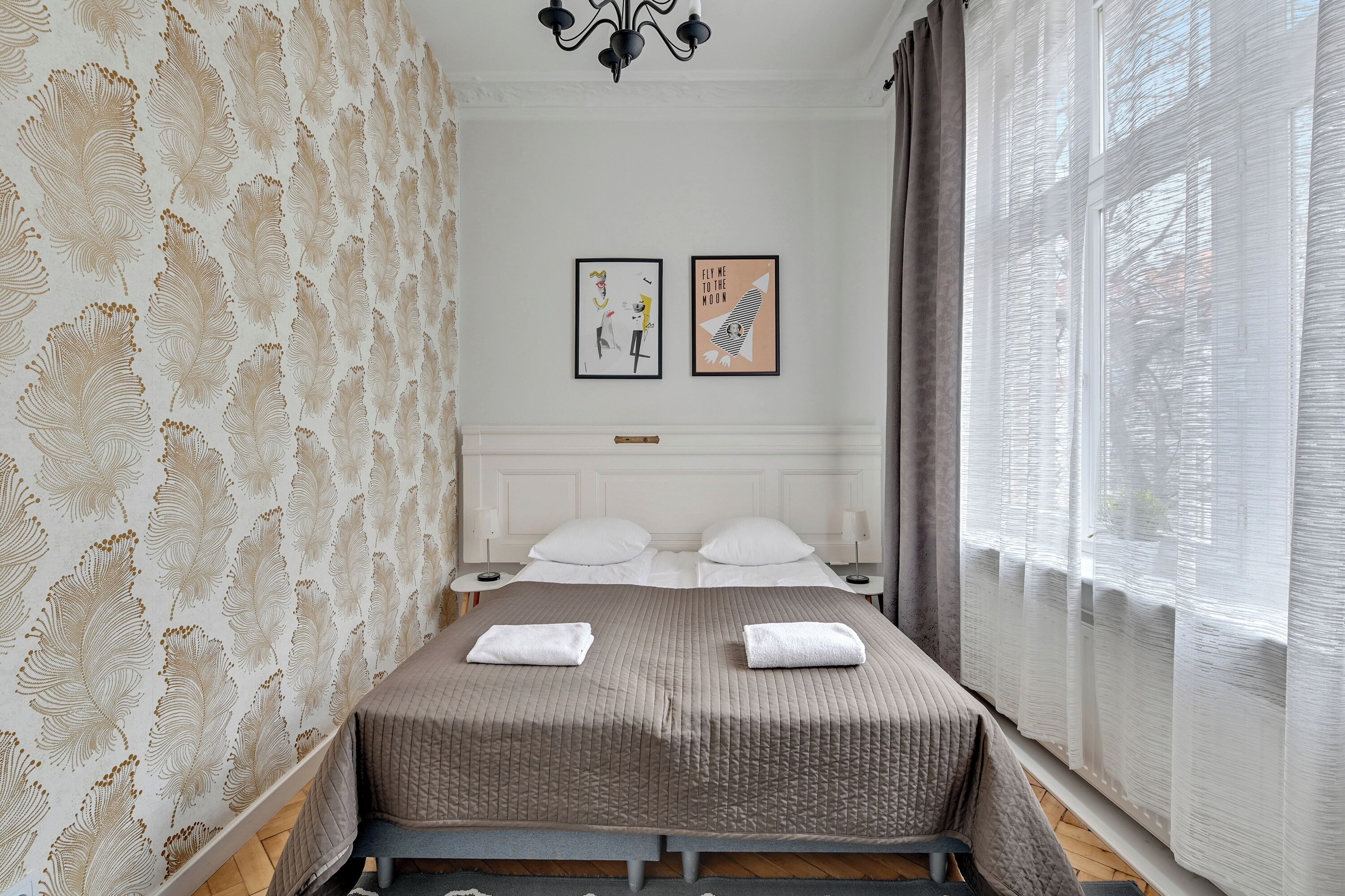 A bedroom with a bed, two framed pictures, and a window with curtains.