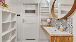 Une salle de bain avec une porte blanche, un meuble-lavabo en bois, un miroir rond et des carreaux décorés.