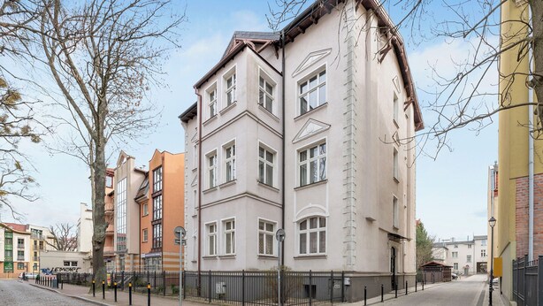 Un immeuble à plusieurs étages, avec une entrée située à l’angle, une entrée au rez-de-chaussée bien visible et une rue pavée de briques.