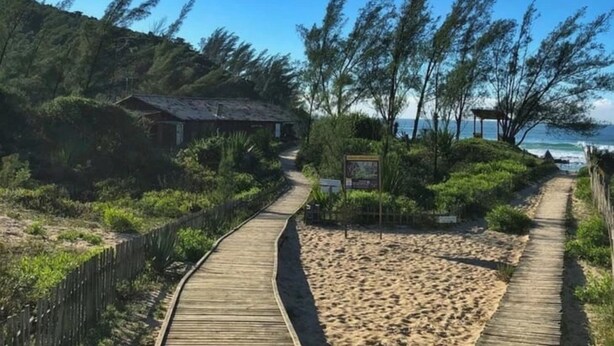 Une promenade en bois menant à une plage, avec un petit bâtiment et un panneau d’affichage.