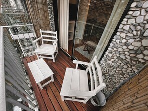 A wooden deck with white chairs and a table, overlooking a stone wall and a garden. - RentUp Zona Jardin botanico balcon (Buenos Aires)