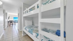 A room with bunk beds, a dining area with chairs and a table, and a view of the sea. - 🦩Book Me Baby! Pelican Isle #604 Penthouse Paradise 🦩 (Fort Walton Beach)