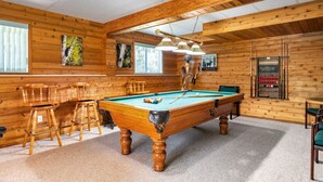Een pooltafel in een ruimte met houten wanden en plafond, barstoelen en een biljarthouder.