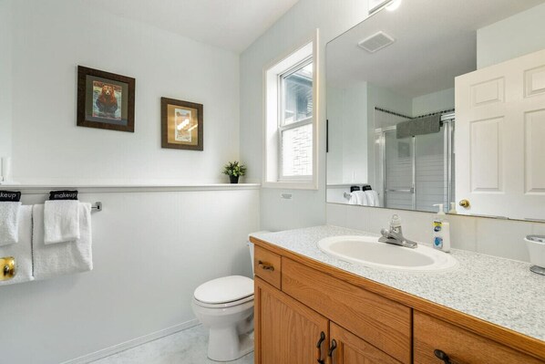 A bathroom with a white toilet, a wooden vanity with a sink, a large mirror, and two framed pictures on the wall.