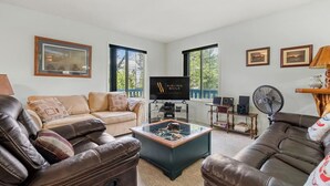 Een woonkamer met een leren bank, een glazen salontafel, een televisie en ingekaderde foto’s aan de muur.